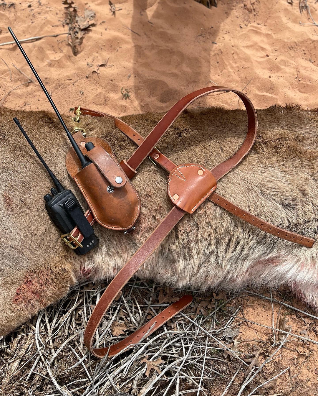 Leather Garmin Alpha Harness laid on fur with walkie talkie and long antenna in outdoor setting
